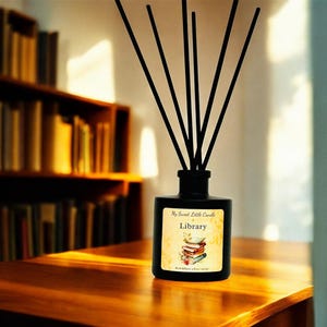 May include: Black diffuser bottle with black reeds, labeled "My Sweet Little Candle Library." The label features a stack of books. The bottle sits on a wooden table, with a bookshelf in the background.