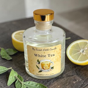 May include: Clear glass reed diffuser with a gold cap, labeled "My Sweet Little Candle White Tea." The label features a teacup illustration. The diffuser is next to lemon slices and green leaves. The diffuser holds 4 fl. oz. / 120 ml.