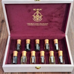 May include: A wooden box with a red velvet interior containing 12 small glass bottles with gold caps. The box has a gold latch and the text "KBN International Perfume Unforgettable Fragrance Unforgettable Moments." is printed on the inside of the lid.