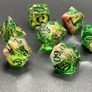 May include: Set of seven polyhedral dice with a green and gold marbled design. The dice are transparent, with black numbering. The dice are for role-playing games.