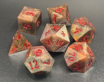 Puede incluir: Conjunto de siete dados poliédricos con un acabado brillante, marrón y dorado. Los números están en rojo. Los dados son para juegos de rol.