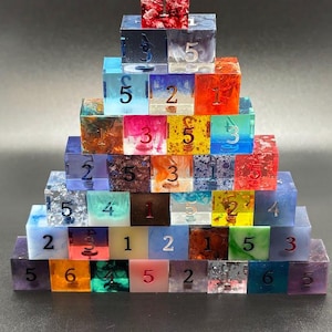 May include: A pyramid of colorful, resin dice with various inclusions and numbers. The dice are arranged in a stepped formation, showcasing a range of colors including red, blue, green, and purple. Each die displays a different number from 1 to 6.