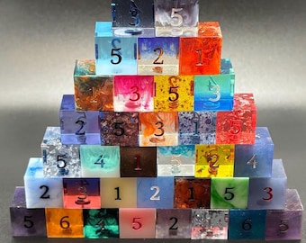 May include: A pyramid of colorful, resin dice with various inclusions and numbers. The dice are arranged in a stepped formation, showcasing a range of colors including red, blue, green, and purple. Each die displays a different number from 1 to 6.