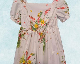 May include: A white dress with a floral print featuring red, yellow, and green flowers. The dress has a square neckline and short puff sleeves.