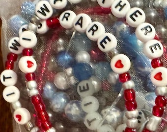 May include: Close-up of a beaded bracelet with white letter beads spelling out the phrase "Will there are" and "Little" with red and silver beads. The beads are on a white background.