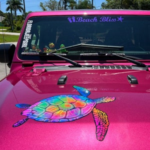 May include: A pink Jeep with a colorful tie-dye turtle decal on the hood. The windshield has a sticker that says "Florida Jeep Girl" and another sticker that says "Beach Bliss" with a purple star.