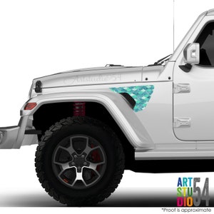 May include: A white Jeep with a teal and blue mermaid scale design on the front fender. The text "Artstudio54" is written on the hood. The vehicle has black tires and red suspension springs.