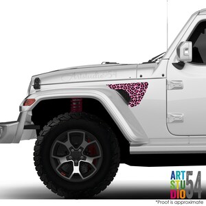 May include: A white Jeep with a pink leopard print decal on the front fender. The decal is a triangular shape with black and pink spots. The vehicle has black tires and a red suspension.