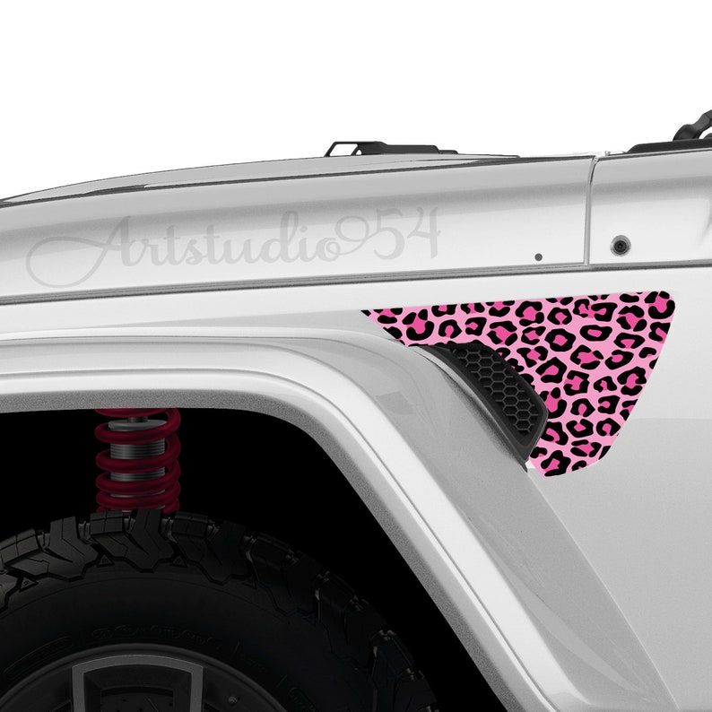 May include: A white vehicle fender with a pink and black leopard print decal. The decal is triangular and covers the vent area. The text "Artstudio954" is visible on the vehicle's body.