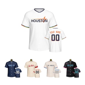 Pode incluir: Camisola de beisebol branca com "HOUSTON" no peito e uma camisola a condizer com "YOUR NAME" e "00" nas costas. Camisolas adicionais apresentam "KANSAS CITY", "Los Angeles", "LOS ANGELES" e "MIAMI" com nomes e números personalizados.