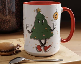 May include: White ceramic mug with a red rim and handle. The mug features a cartoon Christmas tree with a face and arms, wearing red shoes and holding up peace signs. The tree is surrounded by gold stars and a small gold ornament with a face.