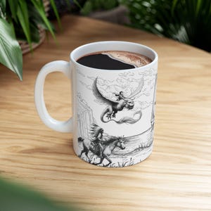 Peut inclure: Une tasse en céramique blanche avec une anse noire. La tasse présente une illustration en noir et blanc d'une créature mythique volant avec une personne à son dos. L'illustration comprend également une personne à cheval au premier plan.