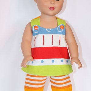 Puede incluir: Una mu&ntilde;eca con un atuendo a rayas de colores con un top sin mangas rojo, blanco, azul y verde y pantalones cortos a juego. La mu&ntilde;eca tiene el pelo casta&ntilde;o y los ojos marrones.