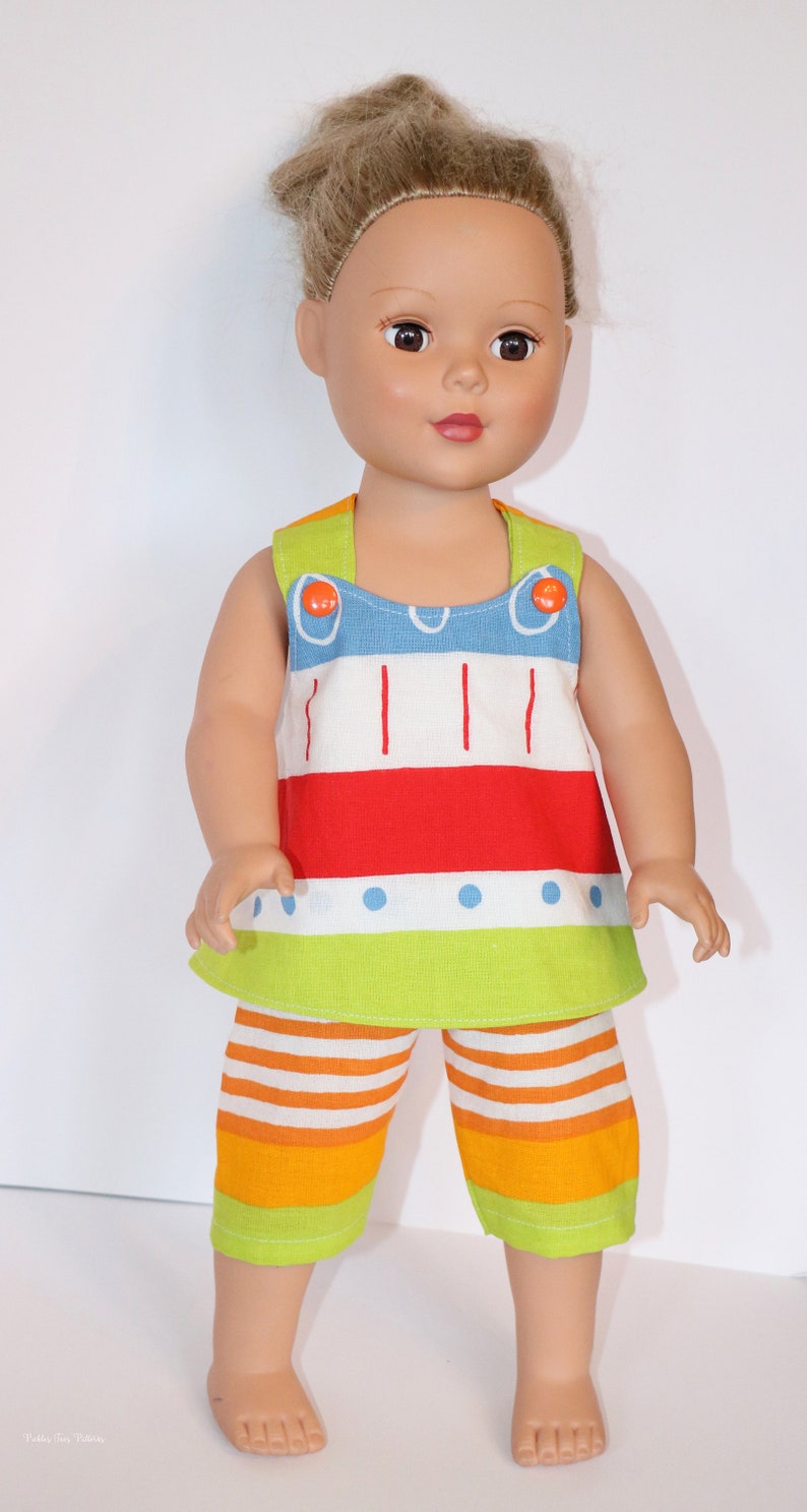Puede incluir: Una mu&ntilde;eca con un atuendo a rayas de colores con un top sin mangas rojo, blanco, azul y verde y pantalones cortos a juego. La mu&ntilde;eca tiene el pelo casta&ntilde;o y los ojos marrones.