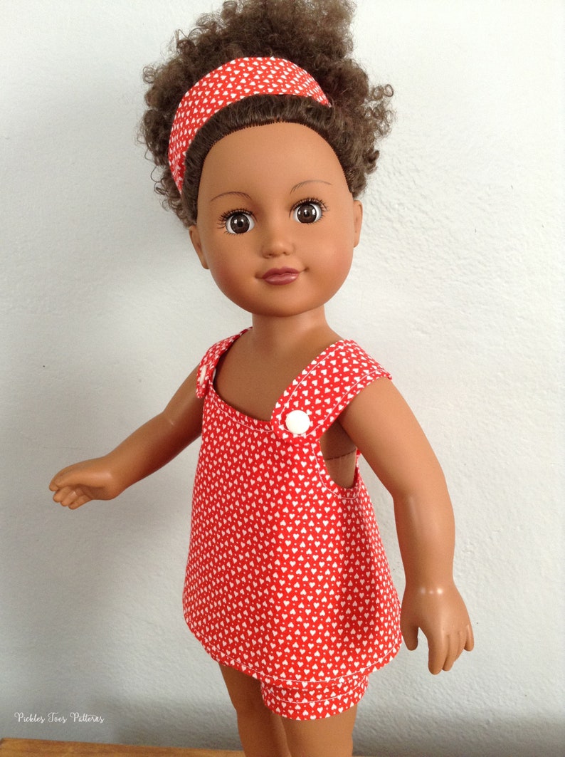 Puede incluir: Una mu&ntilde;eca con un vestido rojo con estampado de corazones blancos y una diadema roja. La mu&ntilde;eca tiene el pelo rizado marr&oacute;n y los ojos marrones.