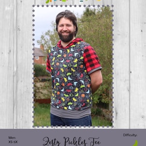 May include: A short-sleeved hooded tee shirt with a black background and colorful dinosaur pattern. The sleeves and hood are red and black plaid. The text "Zesty Pickles Tee" is below the image.