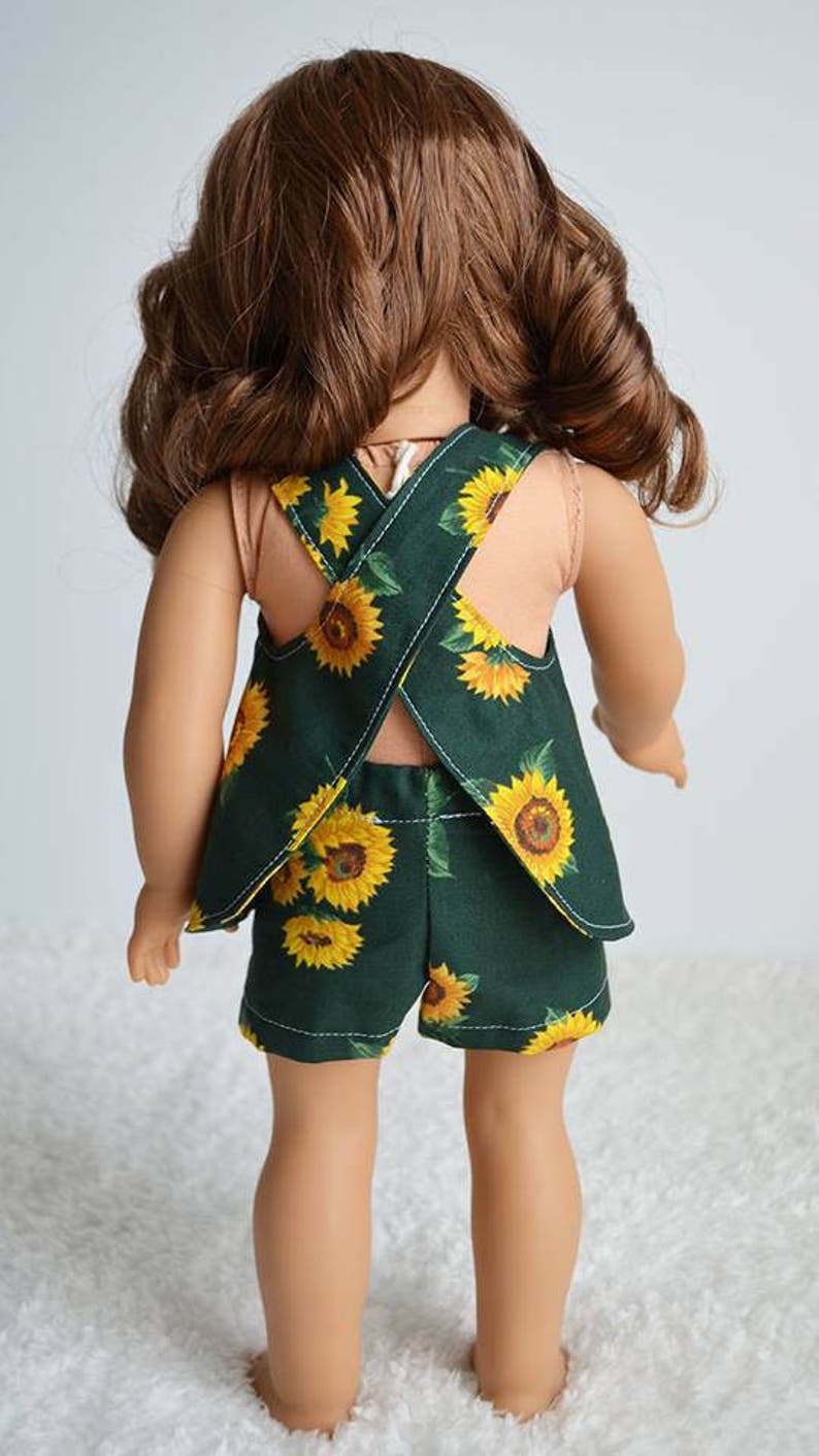 Puede incluir: Una mu&ntilde;eca con un vestido de verano de estampado de girasol verde y amarillo con espalda cruzada. El vestido tiene un dobladillo con volantes y se combina con pantalones cortos a juego.