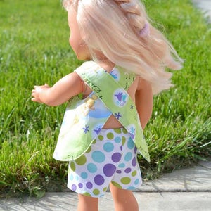 Puede incluir: Una mu&ntilde;eca con un vestido de lunares verdes y blancos con una blusa de estampado floral verde y blanco. La blusa tiene un dise&ntilde;o de espalda cruzada.