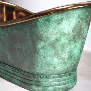 May include: A close-up of a copper bathtub with a verdigris finish. The rim and interior are a polished gold color. The tub has a curved design and a riveted band near the base.