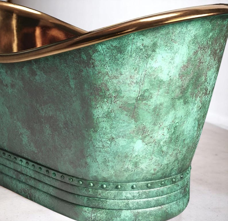 May include: A close-up of a copper bathtub with a verdigris finish. The rim and interior are a polished gold color. The tub has a curved design and a riveted band near the base.