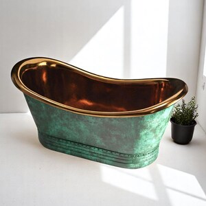 May include: A freestanding bathtub with a copper interior and a green exterior with a distressed finish. The rim is trimmed with gold. A small potted plant sits nearby.