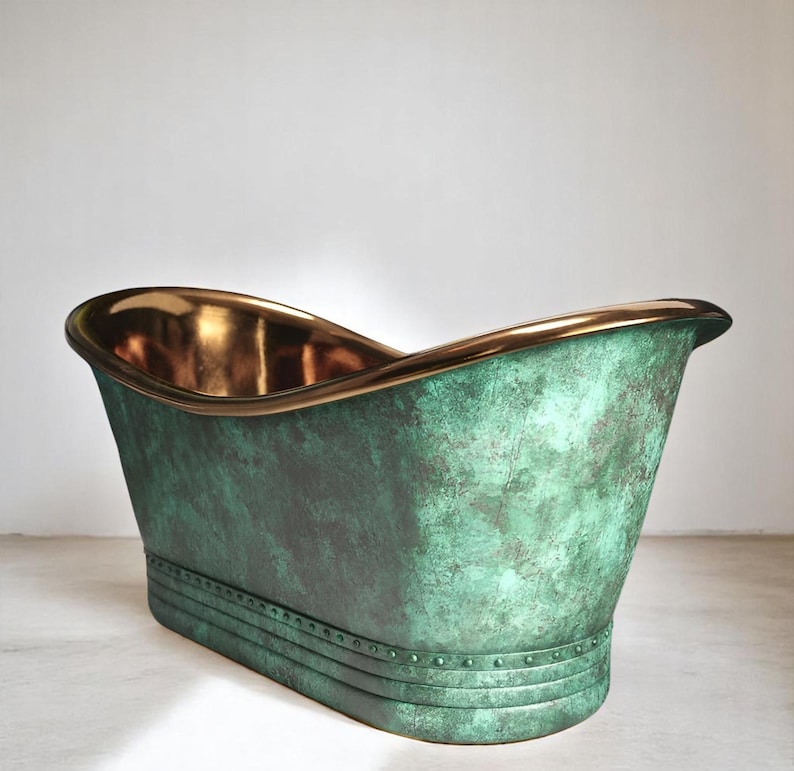 May include: A freestanding bathtub with a weathered green exterior and a polished gold interior. The rim is also gold, and the base has a riveted design. The tub has a classic, elegant shape.