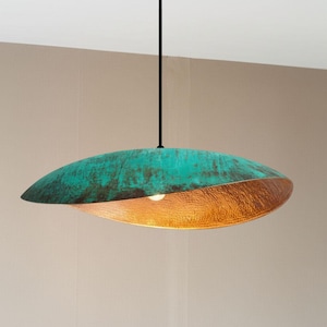 Puede incluir: Una moderna lámpara colgante ovalada con acabado turquesa y cobre. La mitad superior es turquesa con un aspecto texturizado y envejecido, mientras que la mitad inferior es de cobre. La luz cuelga de un cable negro.