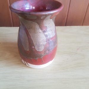 Op de afbeelding: Een kleine, keramische vaas met een bruine, rode en witte glazuur. De vaas heeft een rond lichaam en een geplooide opening.