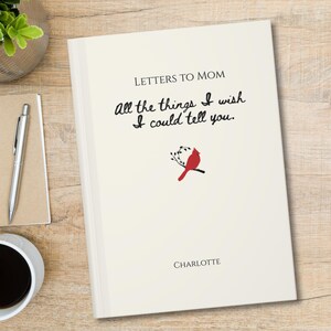May include: A cream-coloured journal with the text "LETTERS TO MOM" and "All the things I wish I could tell you." printed in black. Below the text is a small illustration of a red cardinal bird on a branch, with the name "CHARLOTTE" at the bottom.