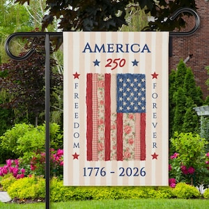 May include: A garden flag with a patriotic design. The flag features the text "AMERICA 250" and the years "1776-2026." It displays a stylized American flag with red and floral stripes and a blue star field. The words "FREEDOM" and "FOREVER" are written vertically.