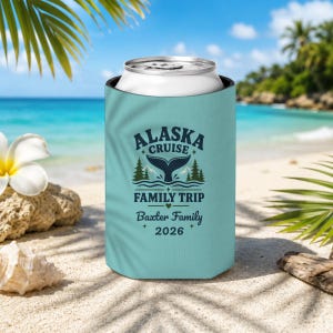 May include: A light blue foam can cooler featuring a dark blue graphic of a whale tail, pine trees, and mountains. The text reads ALASKA CRUISE FAMILY TRIP, Baxter Family, and 2026. The cooler is cylindrical and holds a standard metal beverage can.