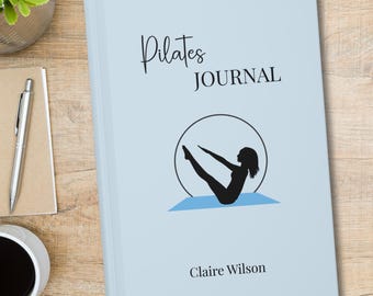 May include: A light blue journal with the text Pilates JOURNAL printed in black. The cover features a black silhouette of a person performing a pilates pose inside a circle, positioned above a blue mat. The name Claire Wilson is printed at the bottom.