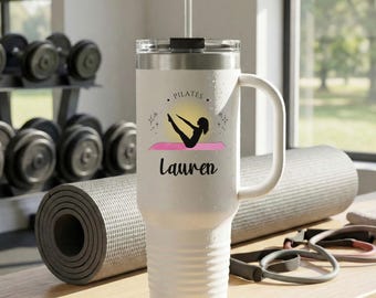 May include: White insulated tumbler with a handle, featuring a Pilates design. The design includes a silhouette of a person doing Pilates on a pink mat, with the name "Lauren" below. The tumbler has a clear lid and a straw.
