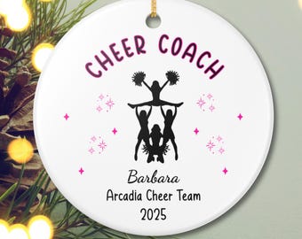 Può includere: Un ornamento natalizio rotondo in ceramica bianca con un cordino dorato per appenderlo. Presenta il testo "CHEER COACH" in rosa, insieme a una silhouette nera di cheerleader. Sono inclusi anche il nome "Barbara", "Arcadia Cheer Team" e l'anno "2025".