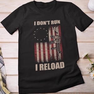 May include: Black t-shirt with a distressed American flag design and the text "I don't run I reload".