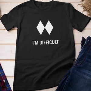 May include: Black t-shirt with two white diamond shapes and the text "I'M DIFFICULT". The design has a distressed effect. The t-shirt is made of a soft material and is suitable for casual wear.