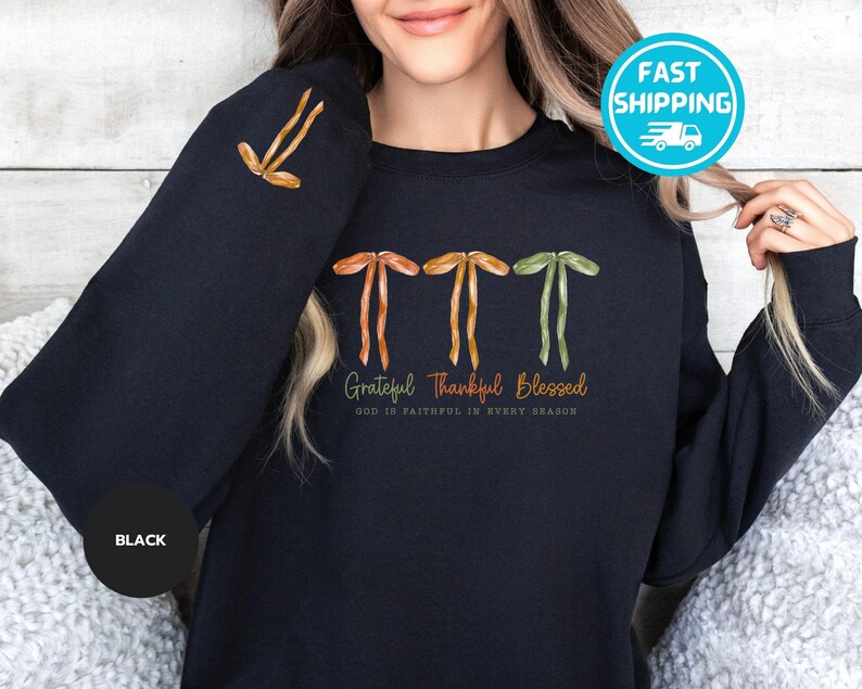Pu&ograve; includere: Felpa nera con le parole "Grateful Thankful Blessed" in corsivo. La felpa presenta tre grafiche stilizzate a farfallino in arancione, giallo e verde. Il testo "GOD IS FAITHFUL IN EVERY SEASON" &egrave; in basso.