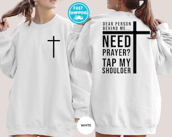 Puede incluir: Sudadera blanca con una cruz negra en la parte delantera y texto en la parte trasera. El texto dice: "DEAR PERSON BEHIND ME... NEED PRAYER? TAP MY SHOULDER." Un pequeño círculo blanco con la palabra "WHITE" está en la parte inferior.