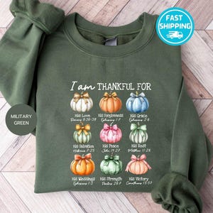 May include: Military green sweatshirt with the text "I am THANKFUL FOR" and colorful pumpkin illustrations. Each pumpkin represents a different blessing, with corresponding Bible verses. The sweatshirt has long sleeves and a crew neck.