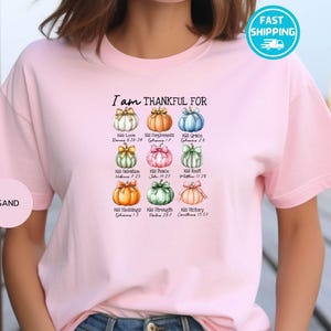 May include: Light pink t-shirt with the text "I am THANKFUL FOR" above nine colorful pumpkin illustrations. Each pumpkin has a different color and is labeled with a word and a Bible verse.