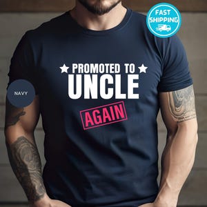 May include: A navy blue t-shirt with white text that reads "Promoted to Uncle Again" with a pink rectangle around the word "Again".