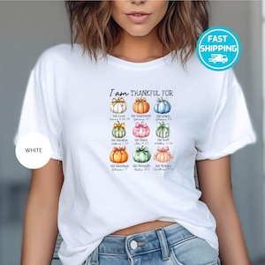 May include: White t-shirt with the text "I am THANKFUL FOR" above a grid of nine colorful pumpkins, each with a different bow and a corresponding Bible verse. The shirt has a round white label that says "WHITE" on it.