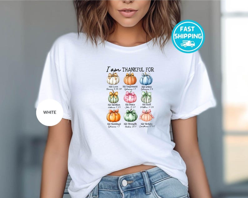 May include: White t-shirt with the text "I am THANKFUL FOR" above a grid of nine colorful pumpkins, each with a different bow and a corresponding Bible verse. The shirt has a round white label that says "WHITE" on it.