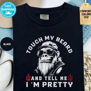 Puede incluir: Camiseta negra con un gráfico de un gorila con gafas de sol y sombrero, con el texto "TOUCH MY BEARD AND TELL ME I'M PRETTY". La camiseta tiene cuello redondo y mangas cortas.