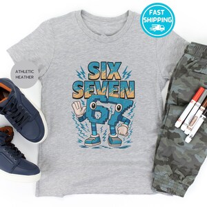May include: A gray athletic heather t-shirt with the words "SIX SEVEN" in blue and orange. The shirt is paired with camouflage pants and blue sneakers. Markers are also included in the image.