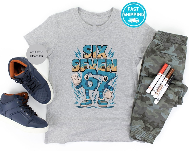 May include: A gray athletic heather t-shirt with the words "SIX SEVEN" in blue and orange. The shirt is paired with camouflage pants and blue sneakers. Markers are also included in the image.