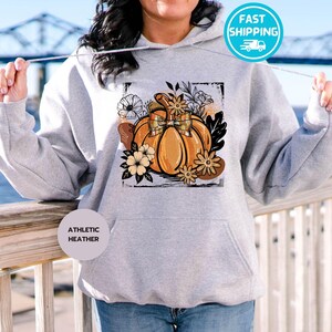May include: Athletic heather gray hoodie with a pumpkin graphic. The pumpkin is orange with a bow and surrounded by flowers and leaves. The hoodie has a front pocket and a drawstring hood.