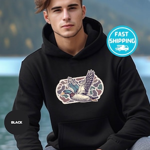 Peut inclure: Sweat-shirt &agrave; capuche noir avec un motif camouflage et un graphique d'un canard volant. Le canard est bleu, vert et blanc.