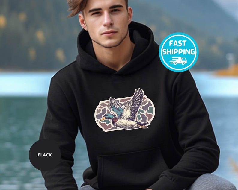 Peut inclure: Sweat-shirt &agrave; capuche noir avec un motif camouflage et un graphique d'un canard volant. Le canard est bleu, vert et blanc.
