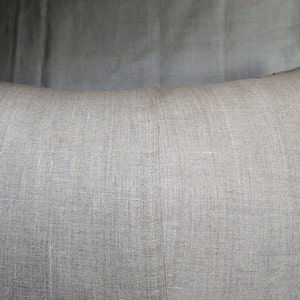 May include: A plain, light gray linen pillow with a subtle texture. The pillow is made of natural fabric and has a simple, understated design.